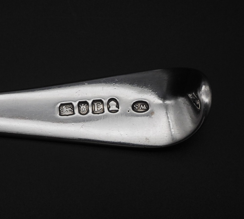 A Georgian sterling silver basting spoon featuring an elongated stem and deep oval bowl on a dark surface. View V