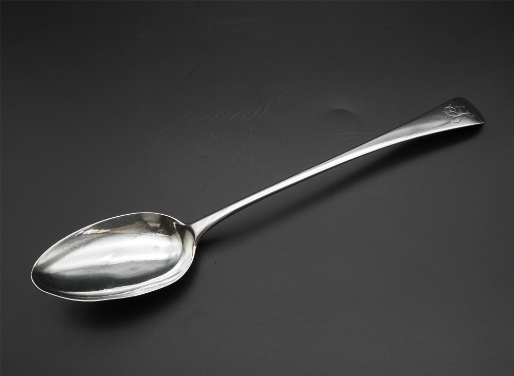 A Georgian sterling silver basting spoon featuring a long tapered handle with an engraved crest and a polished oval bowl. View II