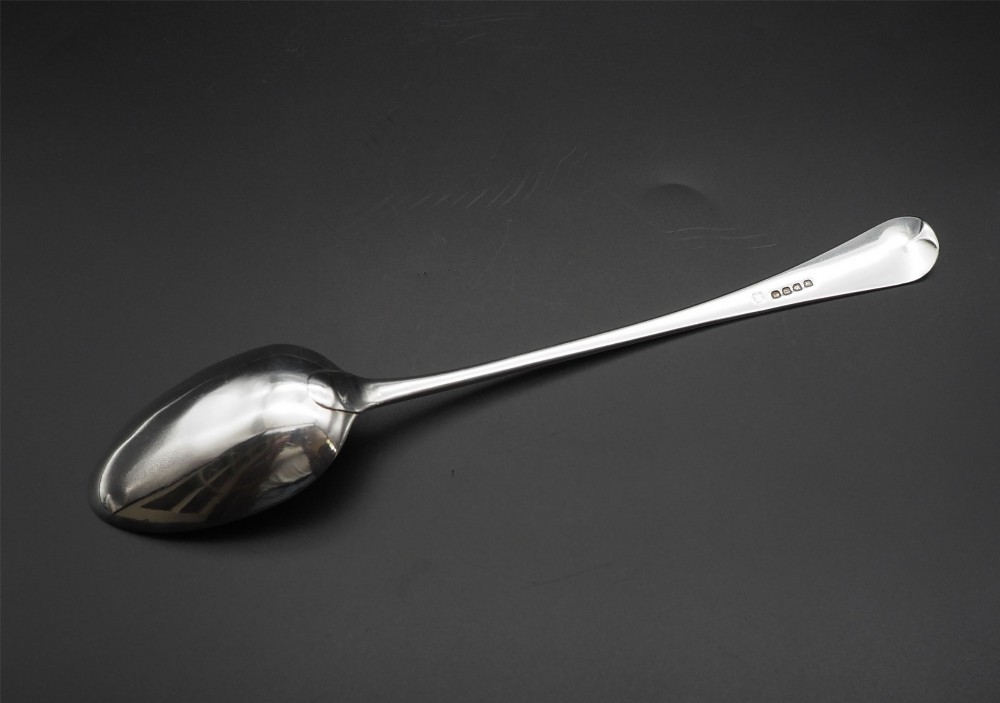 A Georgian sterling silver basting spoon featuring a long tapered handle with an engraved crest and a polished oval bowl. View III