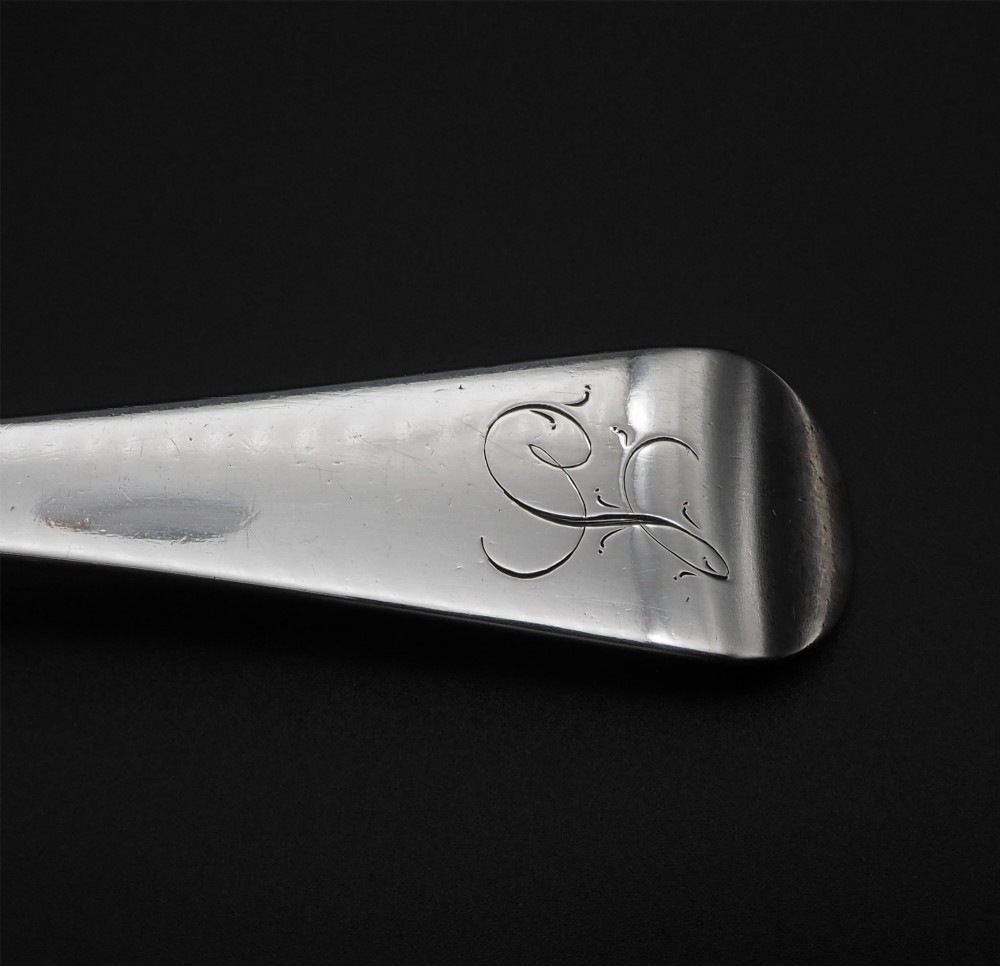 A Georgian sterling silver basting spoon featuring a long tapered handle with an engraved crest and a polished oval bowl. View IV