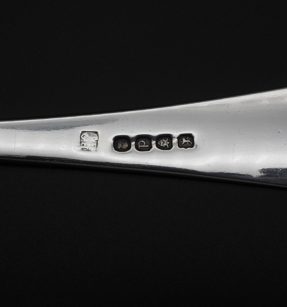 A Georgian sterling silver basting spoon featuring a long tapered handle with an engraved crest and a polished oval bowl. View V