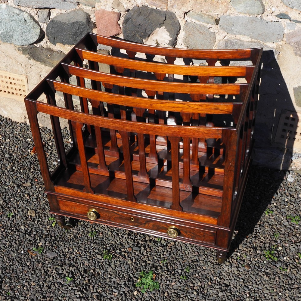 A 19th-century Regency rosewood canterbury with four slatted partitions, vertical supports, a single base drawer, brass knobs, and brass castors.