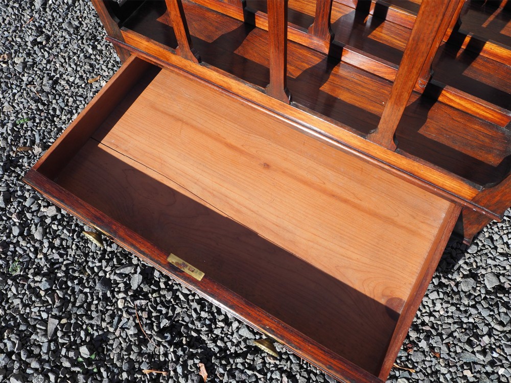 A 19th-century Regency rosewood canterbury with four slatted partitions, vertical supports, a single base drawer, brass knobs, and brass castors. View V
