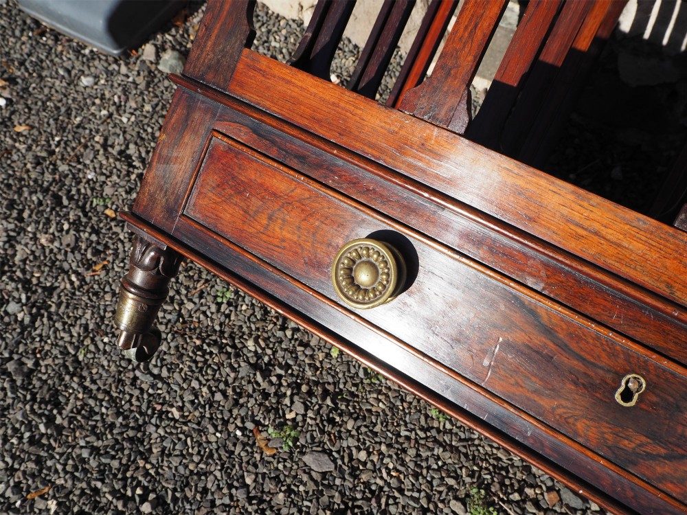 A 19th-century Regency rosewood canterbury with four slatted partitions, vertical supports, a single base drawer, brass knobs, and brass castors. View VI