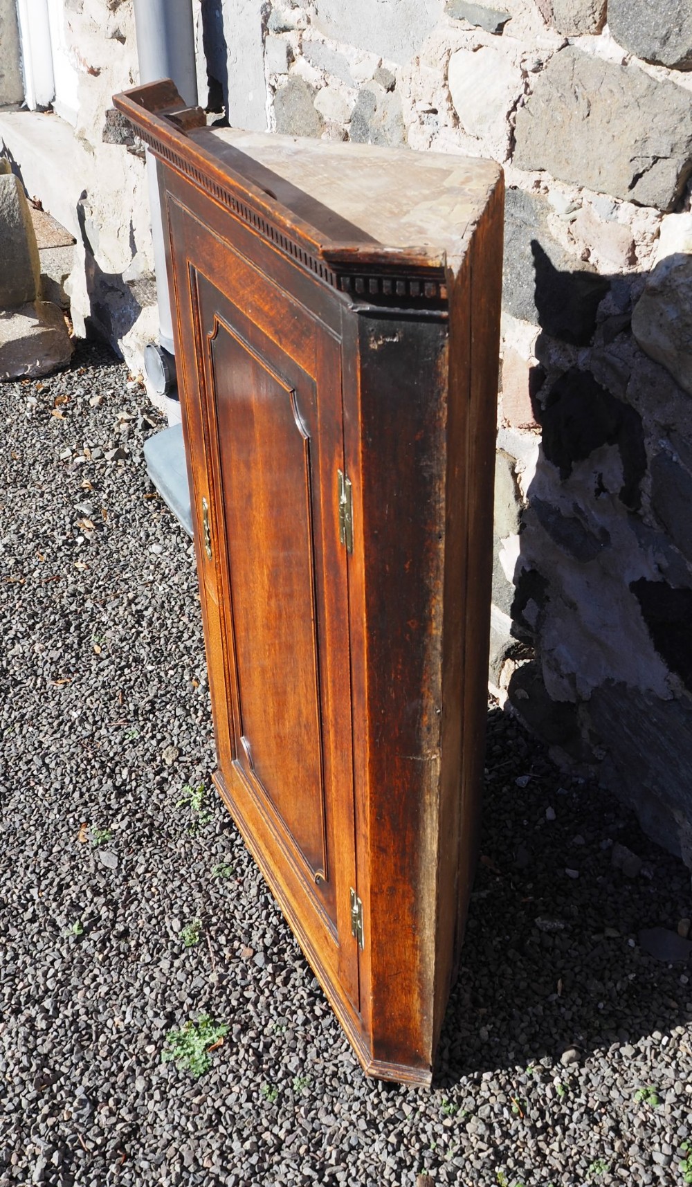 An 18th-century oak corner cabinet featuring a dentil moulded cornice, a single fielded panel door with a brass escutcheon, and brass H-hinges. View III