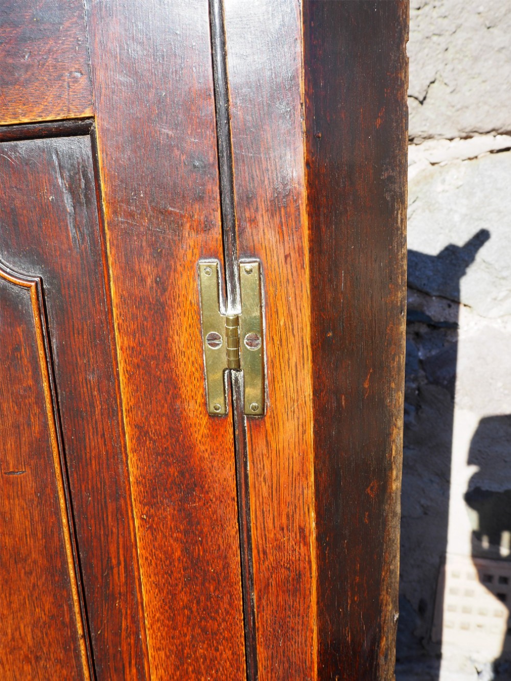 An 18th-century oak corner cabinet featuring a dentil moulded cornice, a single fielded panel door with a brass escutcheon, and brass H-hinges. View V