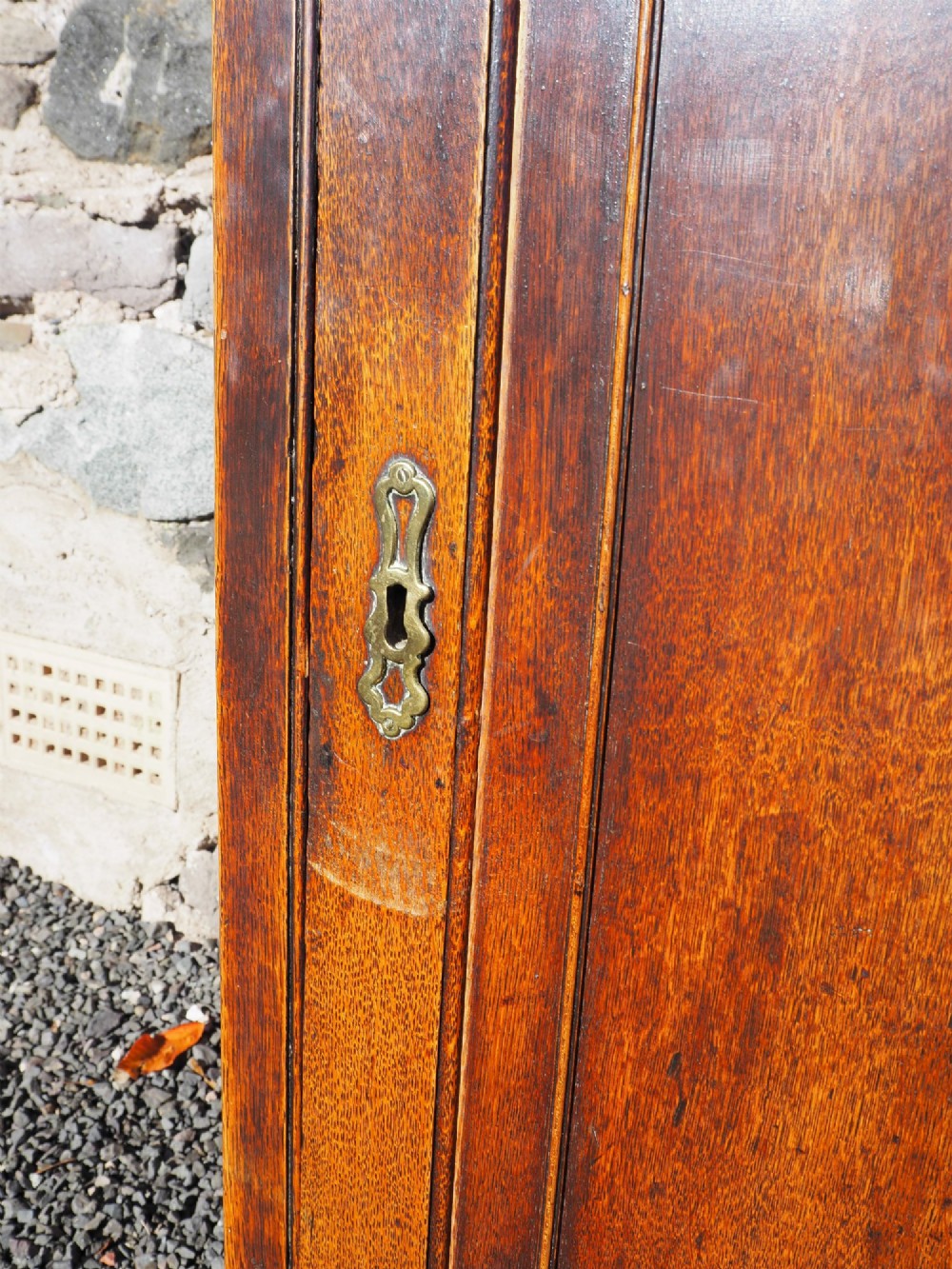 An 18th-century oak corner cabinet featuring a dentil moulded cornice, a single fielded panel door with a brass escutcheon, and brass H-hinges. View VI