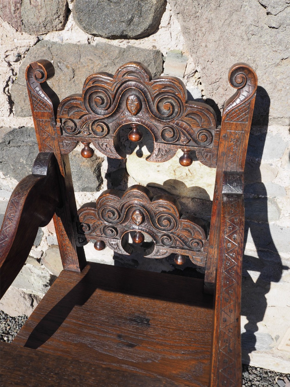 A dark oak childs high chair featuring double carved scroll cresting panels, turned legs, a footrest, and a front bar. View IV