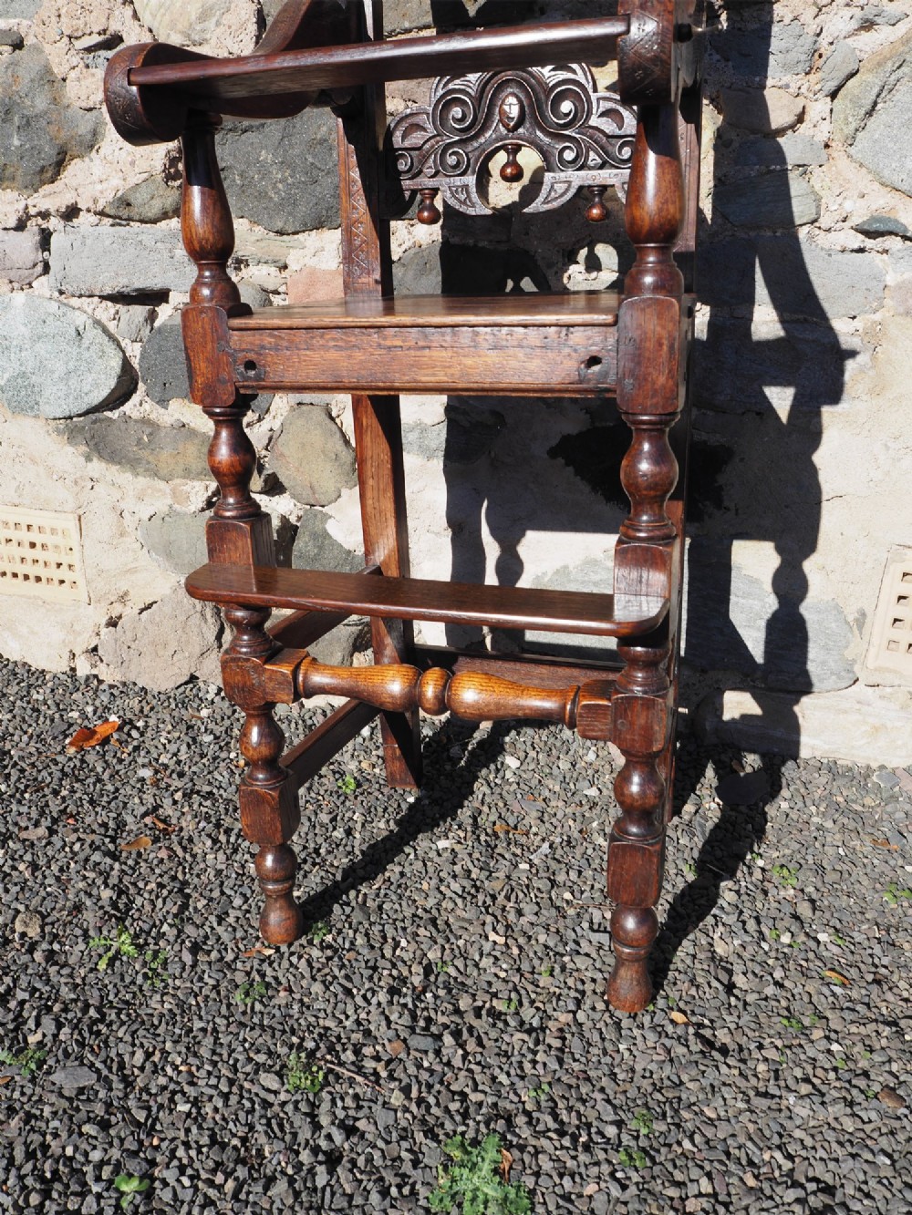 A dark oak childs high chair featuring double carved scroll cresting panels, turned legs, a footrest, and a front bar. View VI