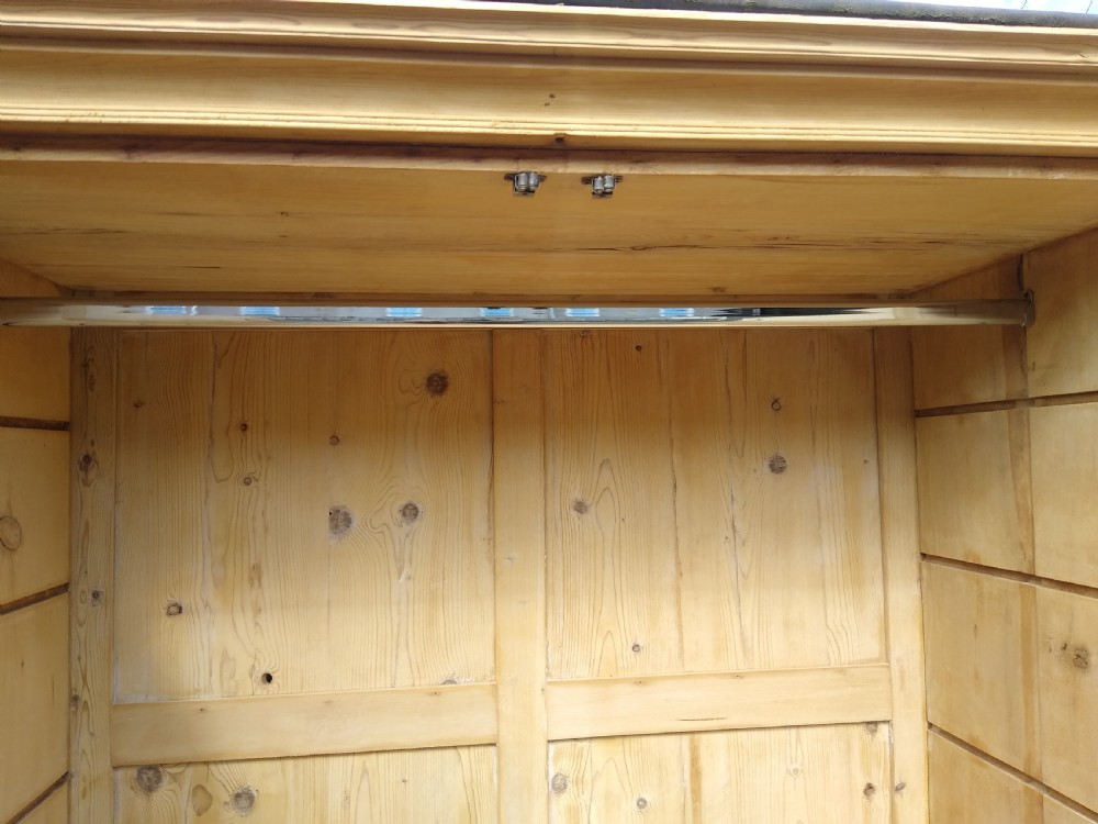 A tall natural pine linen press featuring a two-door upper cupboard above two short drawers and one long drawer with turned wooden knobs. View III