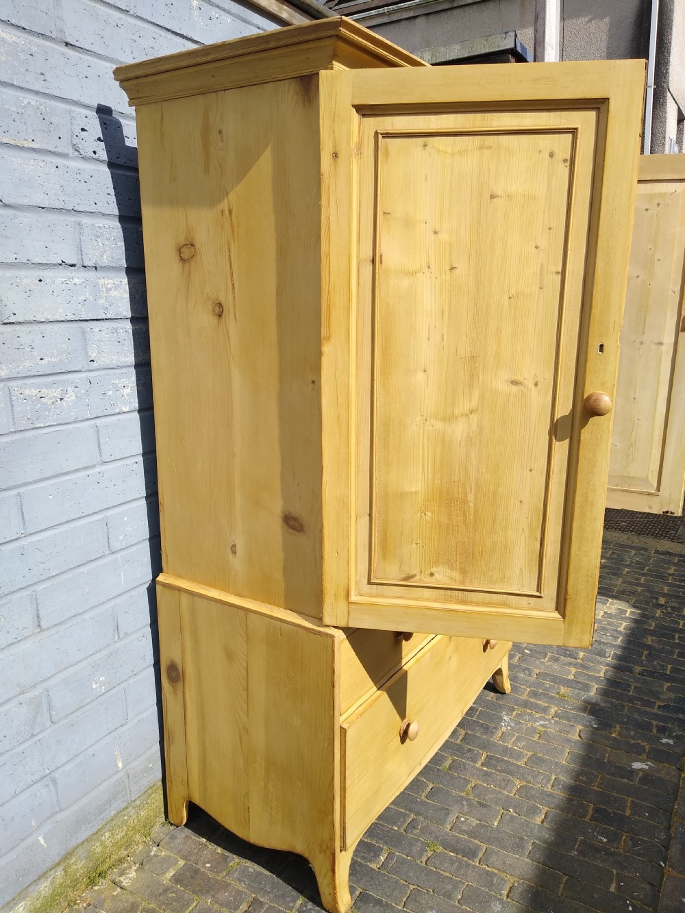 A tall natural pine linen press featuring a two-door upper cupboard above two short drawers and one long drawer with turned wooden knobs. View IV
