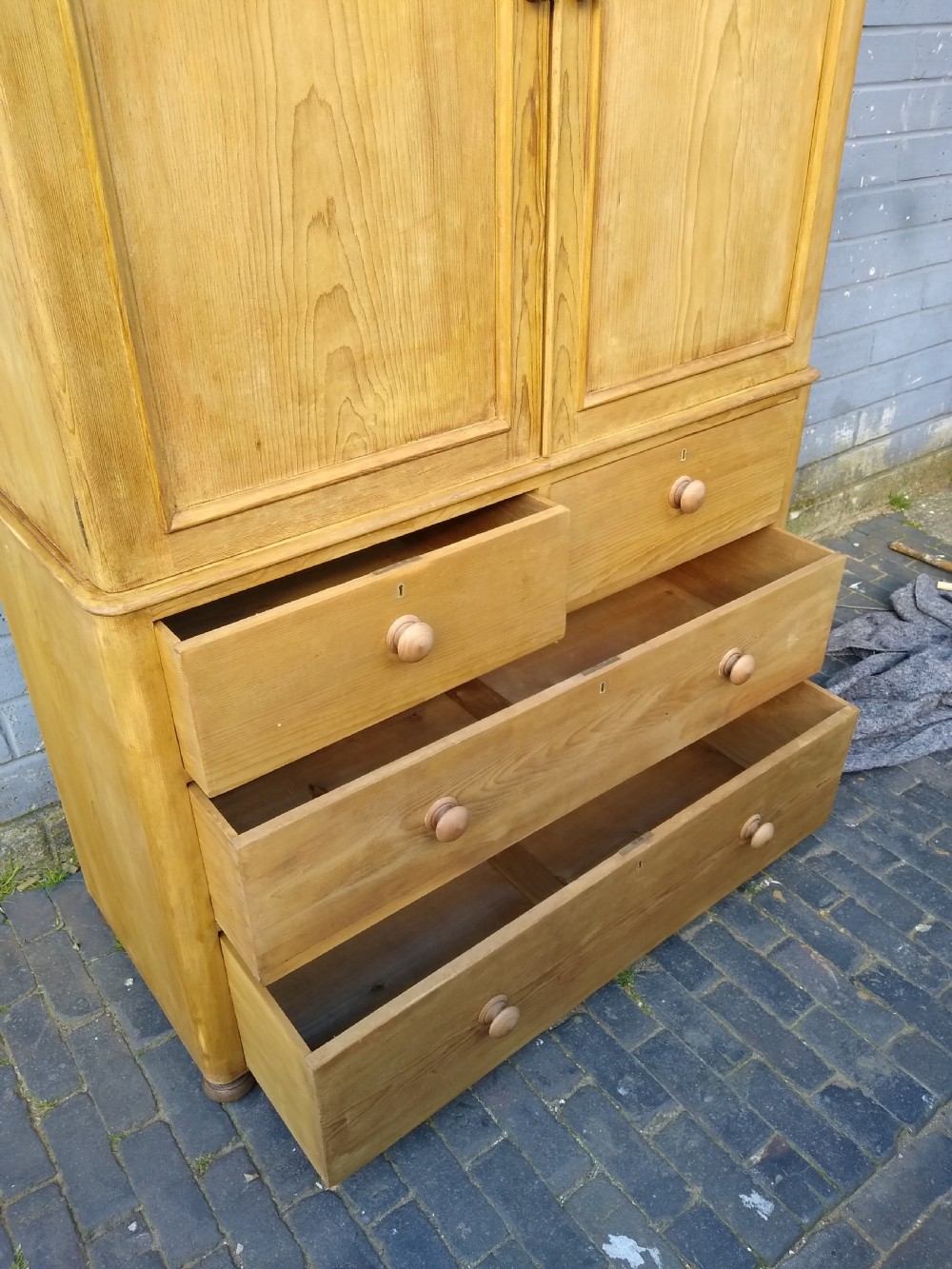 A Victorian rustic pine linen press featuring a moulded top cornice above two arched cupboard doors and a base with four drawers fitted with turned pine knobs. View II