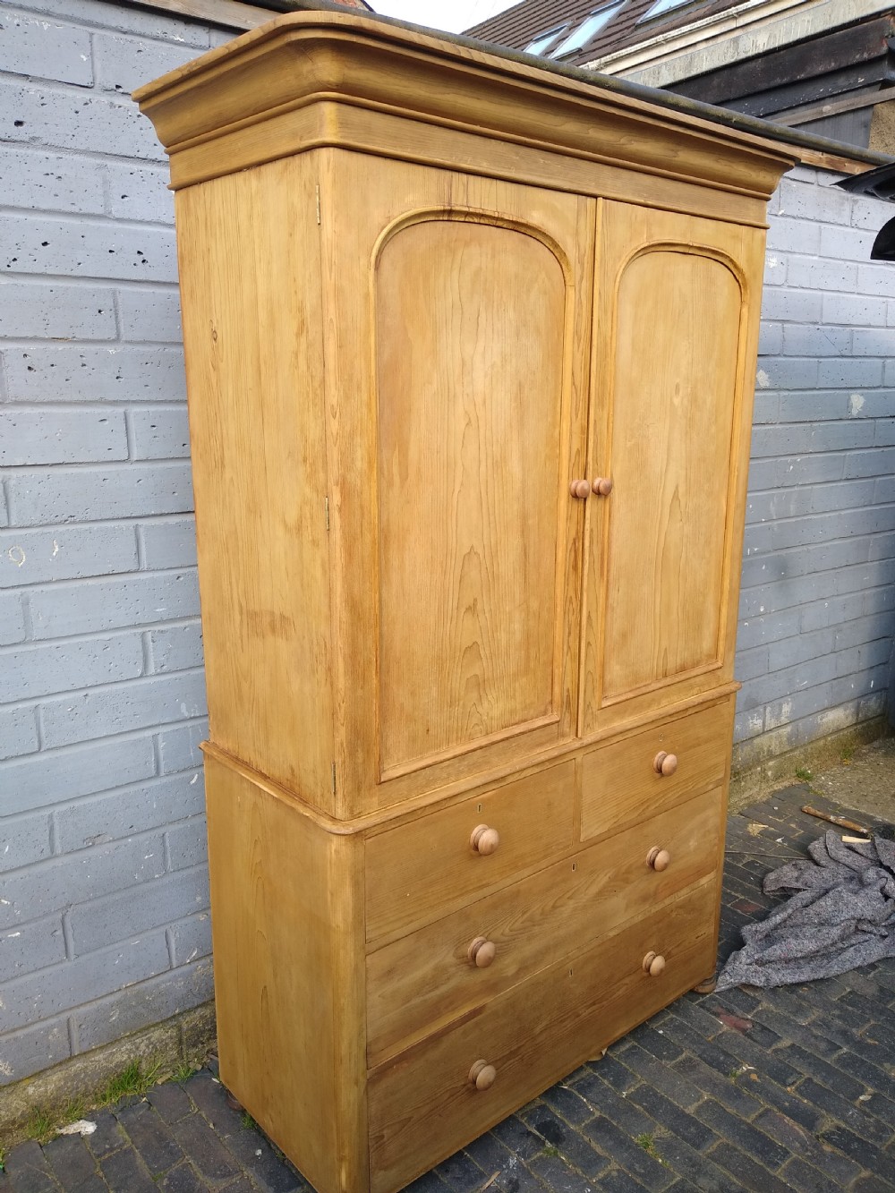 A Victorian rustic pine linen press featuring a moulded top cornice above two arched cupboard doors and a base with four drawers fitted with turned pine knobs. View IV