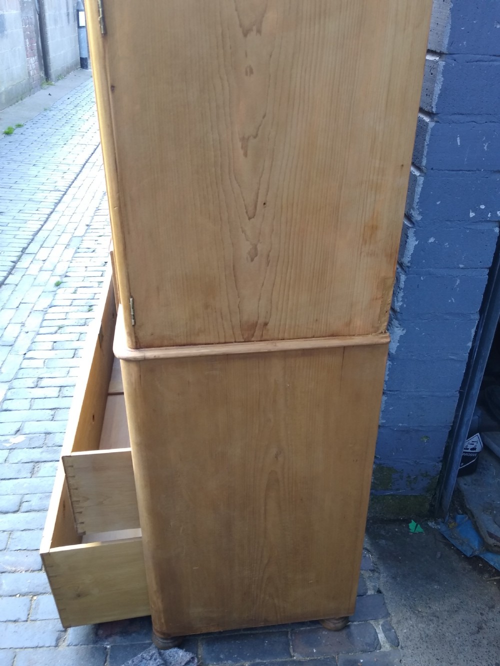 A Victorian rustic pine linen press featuring a moulded top cornice above two arched cupboard doors and a base with four drawers fitted with turned pine knobs. View V