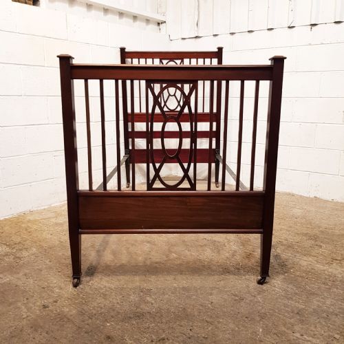 fig 2. A pair of Edwardian mahogany single bed frames featuring slatted headboards and footboards accented with central geometric oval motifs and standing on castors.
