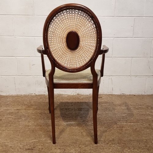 fig 1. A mahogany armchair featuring an oval woven cane back with a central timber medallion, curved armrests, and turned front legs.
