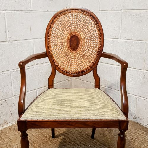 fig 2. A mahogany armchair featuring an oval woven cane back with a central timber medallion, curved armrests, and turned front legs.