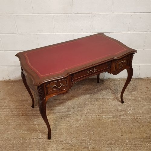 fig 1. A late 19th-century French mahogany writing desk with a serpentine front, red leather inset top, three carved drawers, and slender cabriole legs.