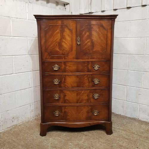 fig 1. A mahogany Chippendale style tallboy featuring upper cupboard doors with shaped moulding over four serpentine-front drawers with brass handles.