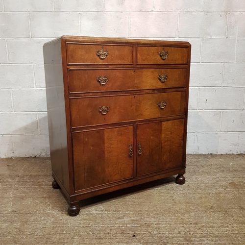 fig 2. A 1920s burr walnut tallboy featuring three upper drawers with brass handles above a double-door cupboard on turned feet.