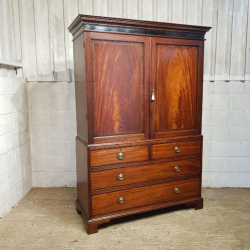 fig 1. A George III mahogany clothes press featuring flame mahogany panelled upper doors above a base with two short and two long drawers on bracket feet.