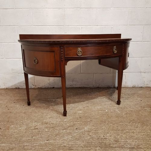 fig 1. An antique mahogany demi-lune side desk featuring a curved front, central drawer with brass ring handles, and tapered square legs.