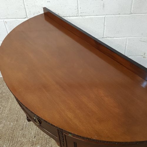 fig 2. An antique mahogany demi-lune side desk featuring a curved front, central drawer with brass ring handles, and tapered square legs.
