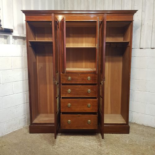 fig 1. An Edwardian mahogany triple wardrobe featuring a central cupboard with urn marquetry above four drawers, flanked by two arched mirrored doors.