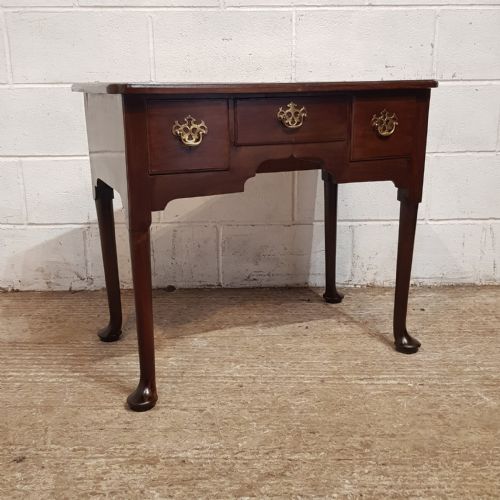 fig 1. A George III dark mahogany lowboy featuring three drawers with brass handles, a shaped apron, and cabriole legs terminating in pad feet.