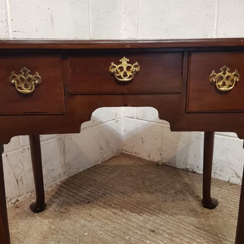 fig 2. A George III dark mahogany lowboy featuring three drawers with brass handles, a shaped apron, and cabriole legs terminating in pad feet.