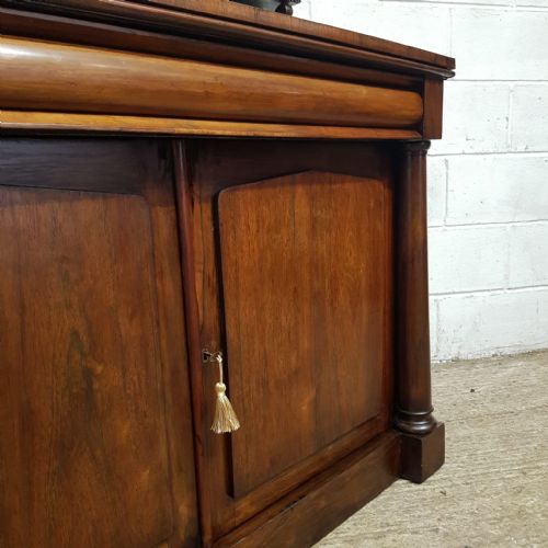 fig 1. An Early Victorian dark rosewood chiffonier featuring a raised shelf upstand with scroll carvings, a cushion drawer, and a two-door lower cabinet flanked by turned columns.