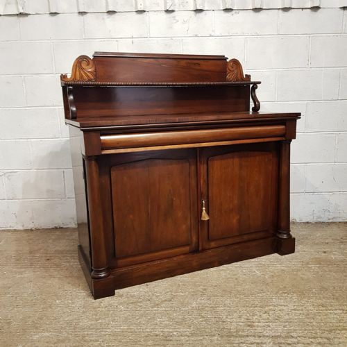 fig 2. An Early Victorian dark rosewood chiffonier featuring a raised shelf upstand with scroll carvings, a cushion drawer, and a two-door lower cabinet flanked by turned columns.