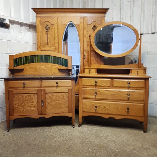 fig 1. A three-piece Edwardian oak bedroom suite comprising a double-door wardrobe with a tall arched mirror, a dressing chest with an oval tilting mirror, and a washstand featuring a dark marble top and green tile splashback.
