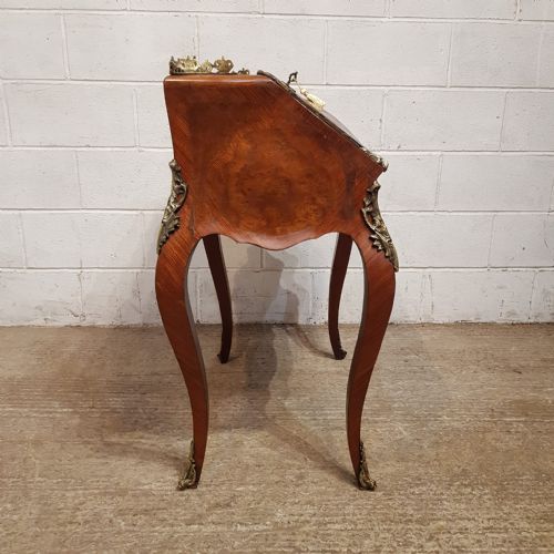 fig 2. A French Louis XV style walnut bureau de dame featuring cabriole legs, a slant-front lid with brass key tassel, decorative brass mounts, and a pierced top gallery.