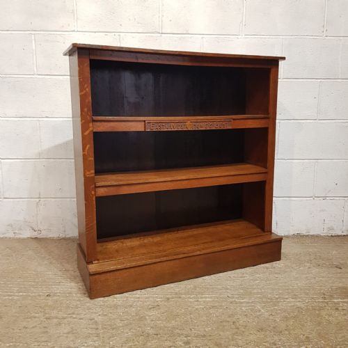 fig 1. A medium brown solid oak open bookcase featuring three shelves with carved lettering along the upper shelf front and a solid plinth base.