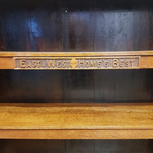 fig 2. A medium brown solid oak open bookcase featuring three shelves with carved lettering along the upper shelf front and a solid plinth base.
