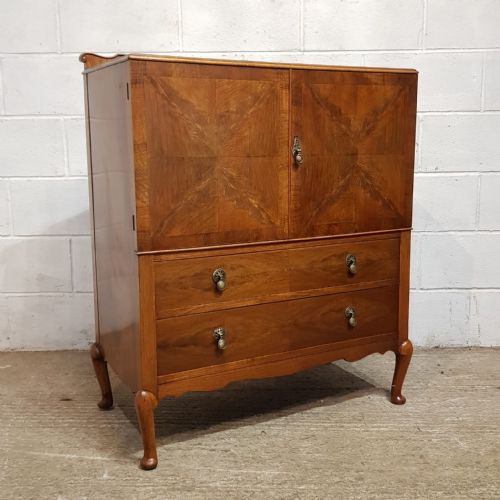 fig 2. A 1920s burr walnut tallboy featuring double cupboard doors with quarter-matched veneer above two drawers, supported by cabriole legs.