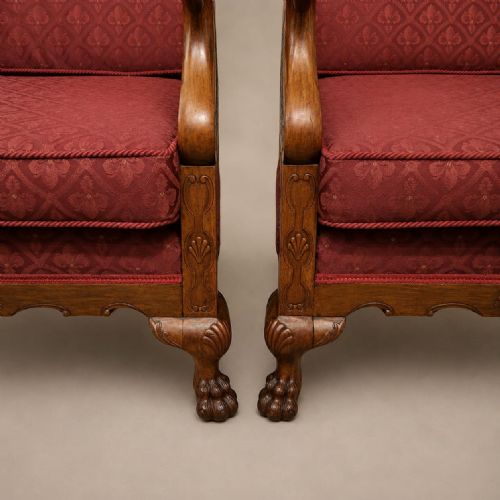 fig 1. A pair of 1920s walnut-framed Bergere armchairs featuring split cane side panels, carved ball and claw feet, and deep red pattern-upholstered cushions.