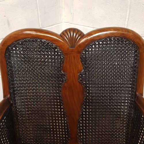 fig 2. A pair of 1920s walnut-framed Bergere armchairs featuring split cane side panels, carved ball and claw feet, and deep red pattern-upholstered cushions.