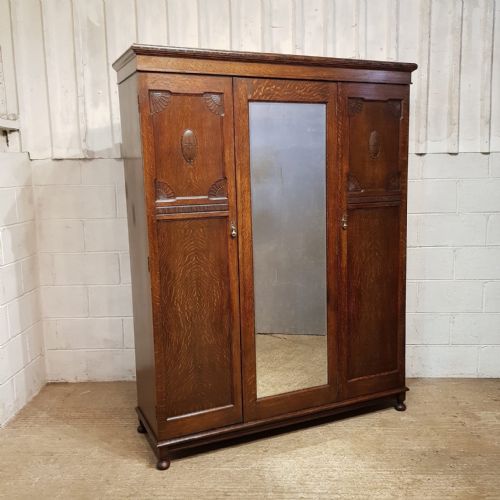 fig 1. A 1920s oak triple wardrobe featuring two carved side doors with oval medallions flanking a central mirrored door.