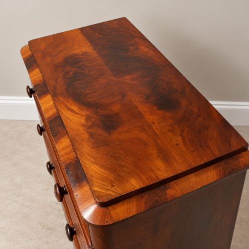 fig 1. A Victorian flame mahogany four-drawer chest featuring turned wooden handles, brass keyhole escutcheons, and rounded side columns.