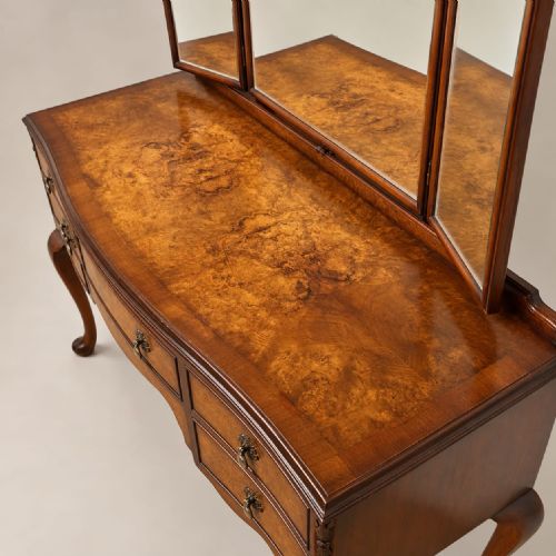 fig 1. A burr walnut Queen Anne style dressing table featuring a serpentine front, five open drawers, brass handles, cabriole legs, and an attached three-piece mirror.