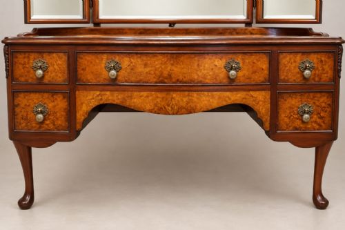 fig 2. A burr walnut Queen Anne style dressing table featuring a serpentine front, five open drawers, brass handles, cabriole legs, and an attached three-piece mirror.