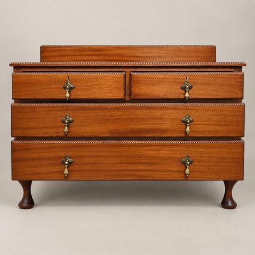 fig 2. An Edwardian mahogany chest of drawers featuring two short over two long drawers, brass drop handles, a low gallery back, and cabriole legs.