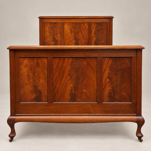 fig 1. An Edwardian mahogany double bedstead featuring flame mahogany panels on the headboard and footboard, raised on front cabriole legs with castors.