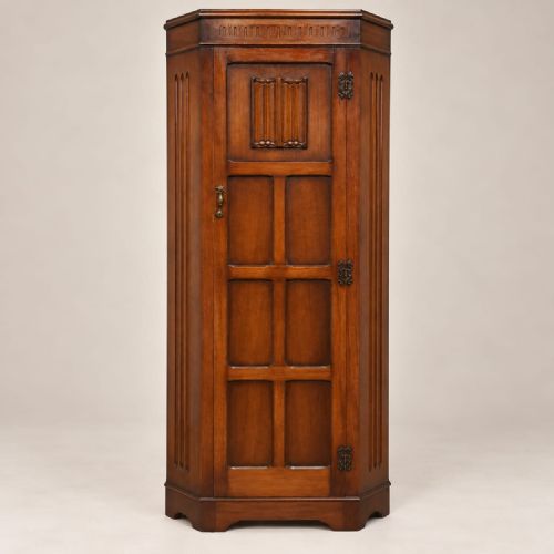 fig 2. A tall brown oak hall wardrobe with a single panelled door featuring carved details, fluted canted corners, and iron hardware.