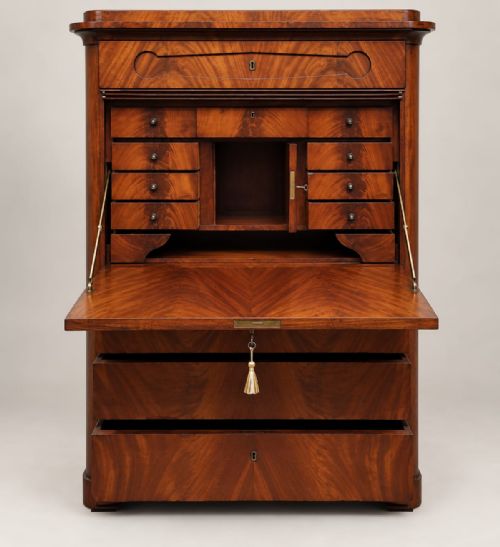 fig 1. A tall 19th-century mahogany Biedermeier secretaire a abattant featuring flame veneer patterns, a central drop-front panel, keyhole escutcheons, and lower drawers.