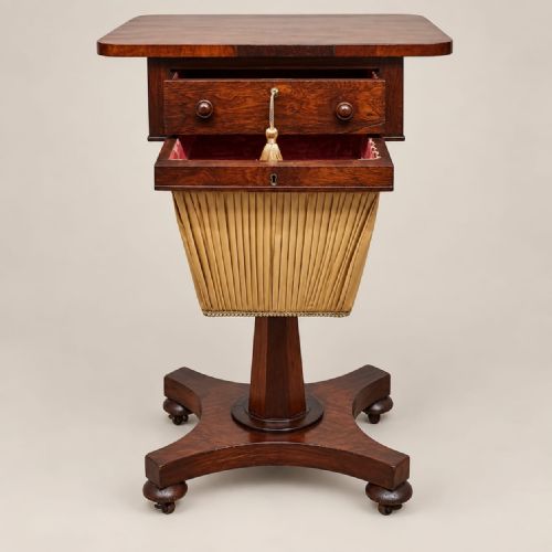 fig 1. A Regency rosewood work table featuring a single drawer with brass keyhole, a pleated yellow fabric basket below, and a quadform base on castors.