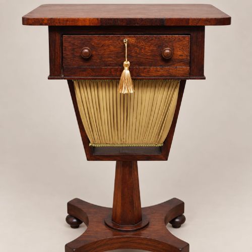 fig 2. A Regency rosewood work table featuring a single drawer with brass keyhole, a pleated yellow fabric basket below, and a quadform base on castors.