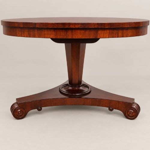 fig 1. An antique circular William IV rosewood tilt-top dining table with a polished surface, central column stem, and triform plinth base with carved scroll feet.